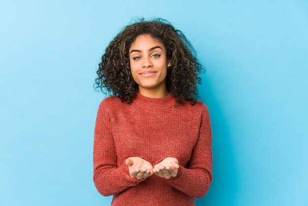 Mujer afroamericana joven del pelo rizado que sostiene algo con las palmas