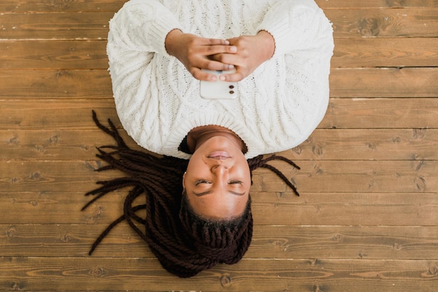 Foto mujer afroamericana joven positiva charlando por teléfono móvil y sonriendo en el suelo en casa yo alegre