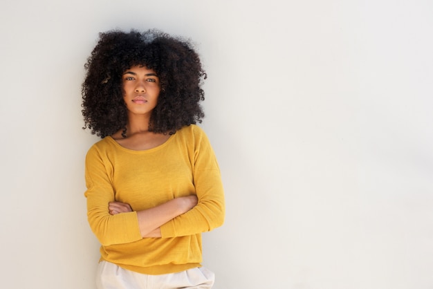 La mujer afroamericana joven que se coloca con los brazos cruzó en el fondo blanco