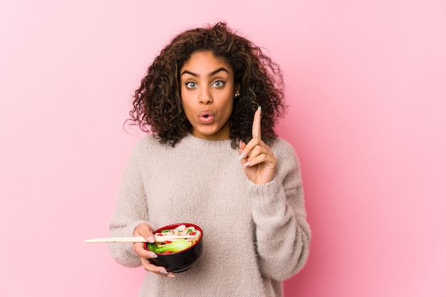 Mujer afroamericana joven que come los tallarines que tienen una gran idea, concepto de creatividad.