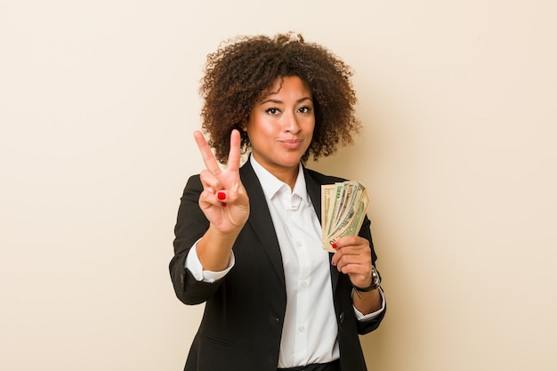 Mujer afroamericana joven que lleva a cabo los dólares que muestran el número dos con los dedos.