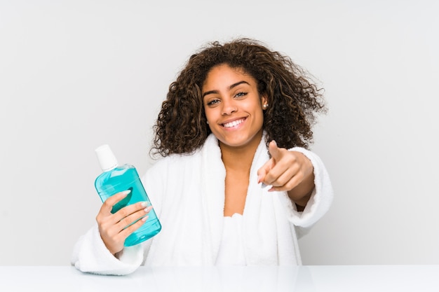 La mujer afroamericana joven que lleva a cabo un enjuague sonríe alegre que señala al frente.