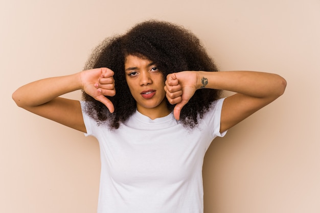 Mujer afroamericana joven que muestra el pulgar hacia abajo y que expresa aversión.