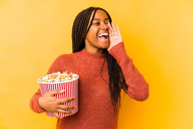 La mujer afroamericana joven que sostenía palomitas aisló gritar y sostener la palma cerca de boca abierta.