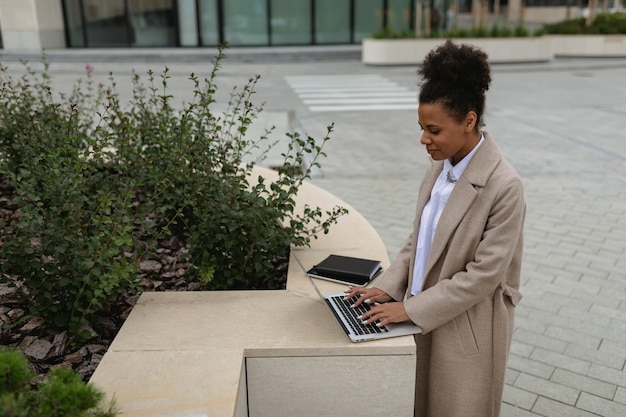 Mujer afroamericana joven que trabaja en la computadora portátil fuera de la oficina