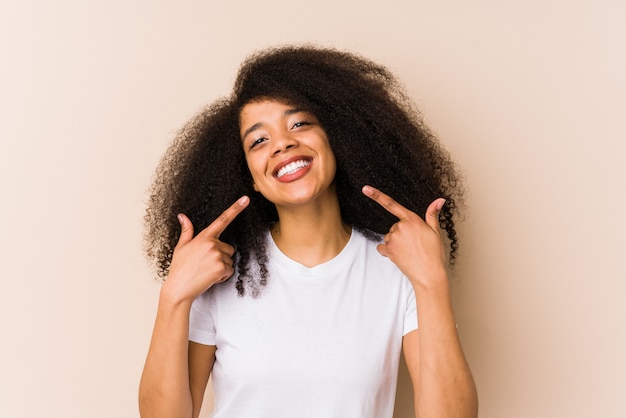 La mujer afroamericana joven sonríe, señalando los dedos en la boca.