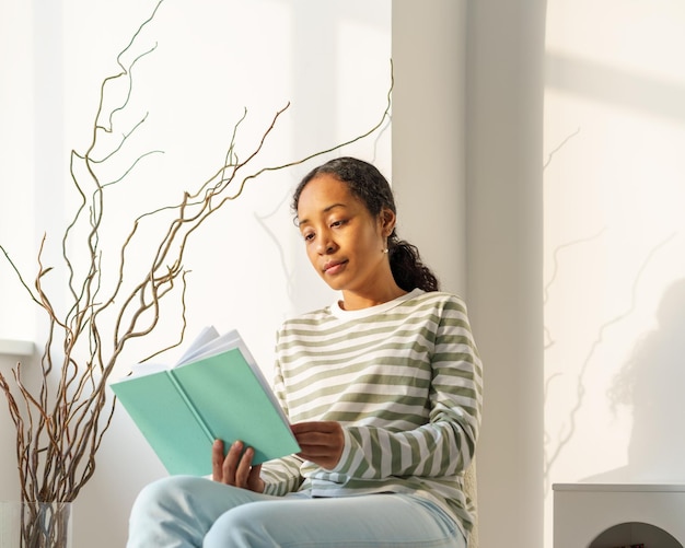 Foto mujer afroamericana leyendo un libro en paz en el salón disfrutando del momento estilo de vida lento