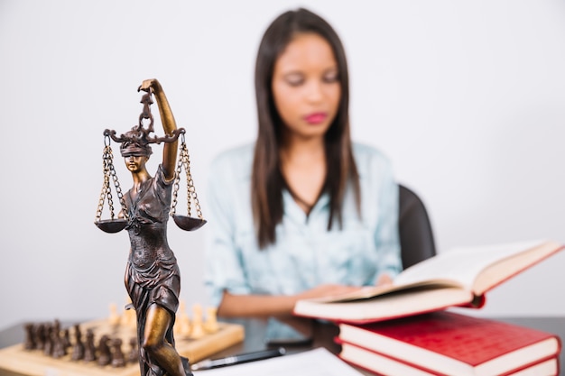 Mujer afroamericana con libro en mesa cerca de ajedrez, teléfono inteligente y estatua