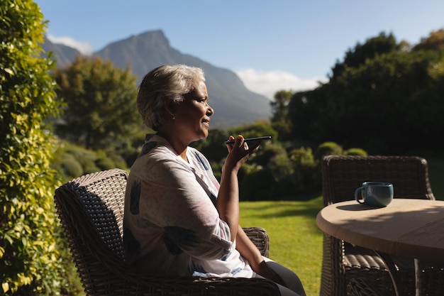 Foto mujer afroamericana mayor hablando por teléfono inteligente en un jardín soleado. concepto de retiro, jubilación y estilo de vida senior feliz.