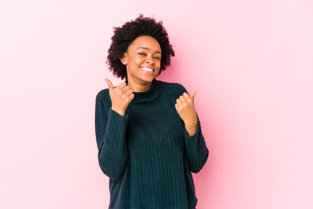 Mujer afroamericana de mediana edad contra una pared rosa aislada levantando ambos pulgares, sonriente y confiada.