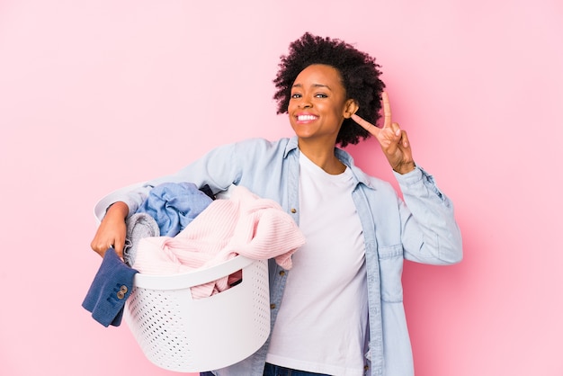 Mujer afroamericana de mediana edad lavando ropa aislada mostrando el signo de la victoria y sonriendo ampliamente.