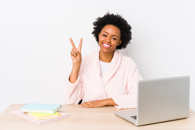 Mujer afroamericana de mediana edad que trabaja en casa aislada mostrando el signo de la victoria y sonriendo ampliamente.