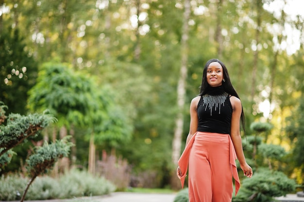 Mujer afroamericana de moda con pantalones de melocotón y blusa negra posa al aire libre.