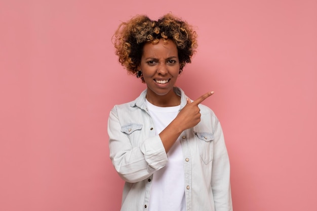 Mujer afroamericana con una mueca triste que señala el pulgar a un lado expresa emociones de arrepentimiento