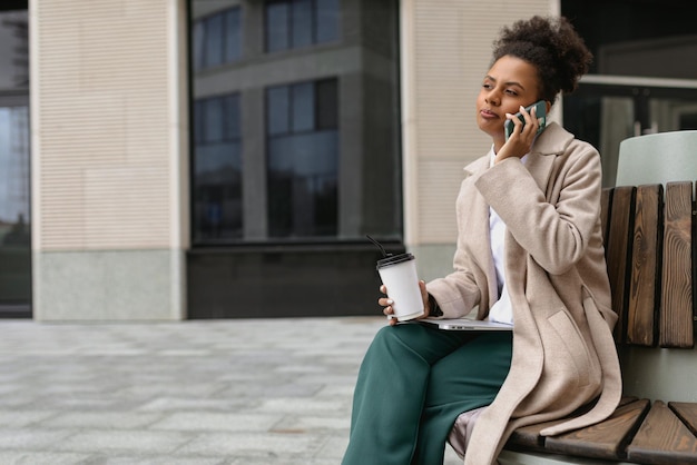 Mujer afroamericana de negocios de treinta años con laptop y teléfono fuera de la oficina