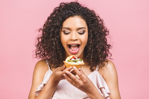 Mujer afroamericana negra feliz con peinado afro rizado haciendo un lío comiendo un postre de lujo enorme