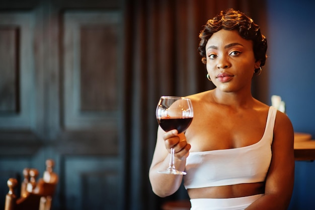 Mujer afroamericana, peinado retro con vestido blanco en el restaurante con copa de vino.