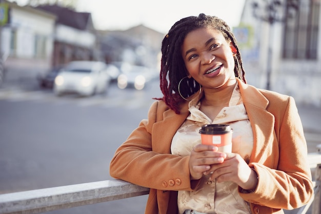 Mujer afroamericana de pie en un srteet con taza de café para llevar