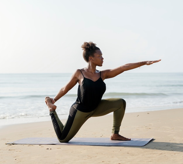 Mujer afroamericana practicando yoga en la playa