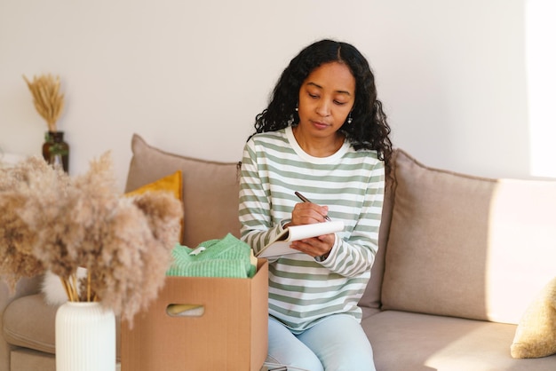 Mujer afroamericana que lleva la cuenta de la ropa en una caja de cartón alejándose y empacando