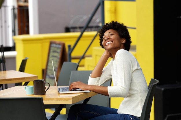 Mujer afroamericana que ríe con la computadora portátil en el café