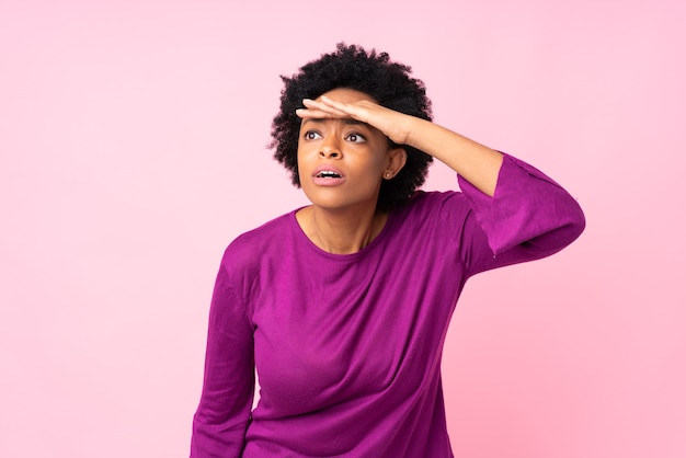 Mujer afroamericana en rosa aislado mirando lejos con la mano para mirar algo