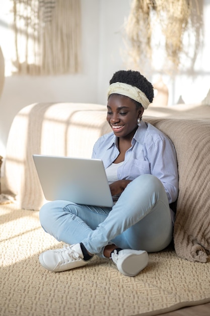 Mujer afroamericana sentada en el sofá y pasando tiempo en el chat en línea