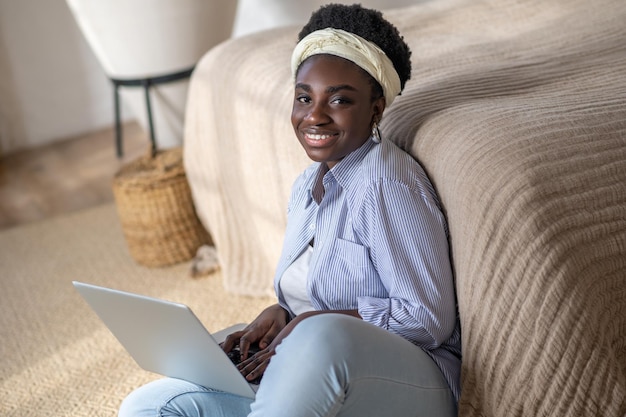 Mujer afroamericana sentada en el sofá y pasando tiempo en el chat en línea