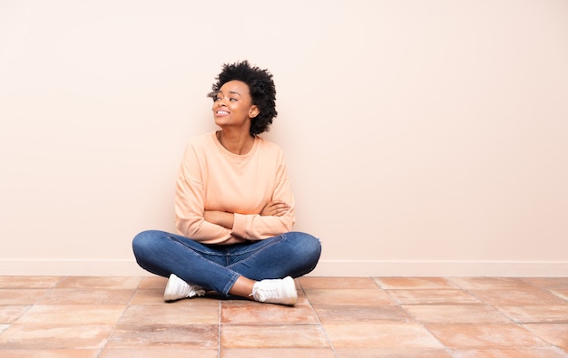 Mujer afroamericana sentada en el suelo con los brazos cruzados y feliz