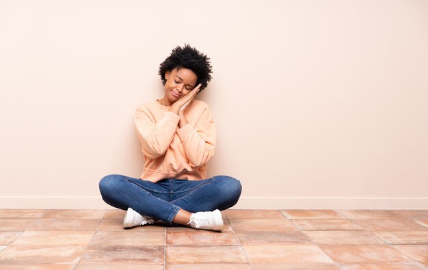 Mujer afroamericana sentada en el suelo haciendo gesto de sueño