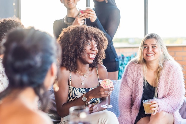 Una mujer afroamericana sentada en una terraza con sus amigos bebiendo y pasando un buen rato.