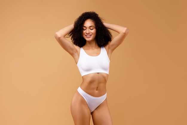 Foto mujer afroamericana sexy posando en ropa interior blanca con los ojos cerrados y las manos detrás de la cabeza