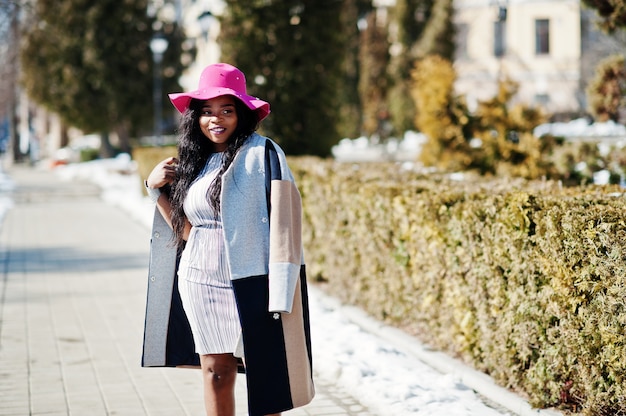 Mujer afroamericana en sombrero y abrigo con teléfono caminando en las calles.