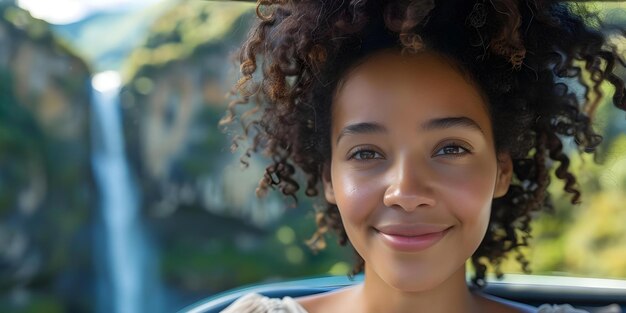 Mujer afroamericana sonriendo en el coche admirando el paisaje de la montaña y la cascada Concepto sesión de fotos al aire libre Mujer africano-estadounidense sonriendo coche paisaje de montaña vista de cascada