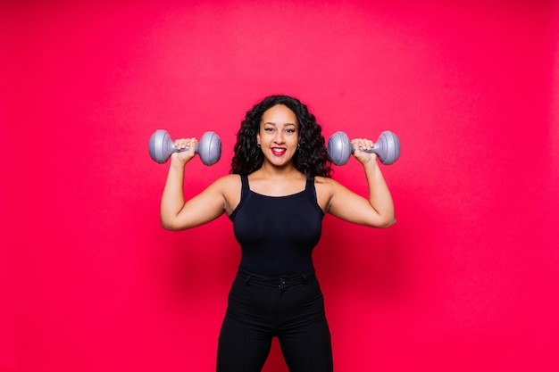 Una mujer afroamericana sonriente haciendo ejercicios de manos con pesas en un fondo de estudio rojo