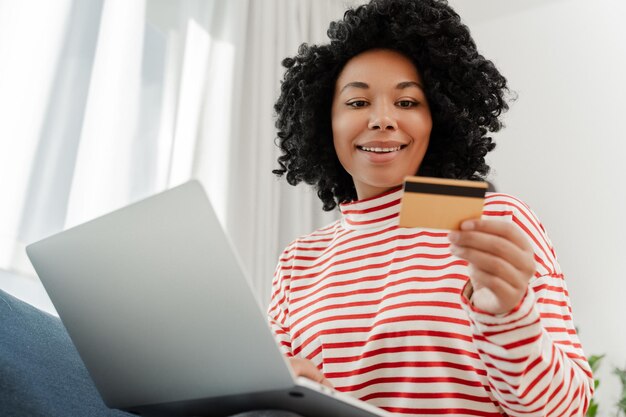 Mujer afroamericana sonriente usando una computadora portátil con tarjeta de crédito comprando en línea pidiendo comida