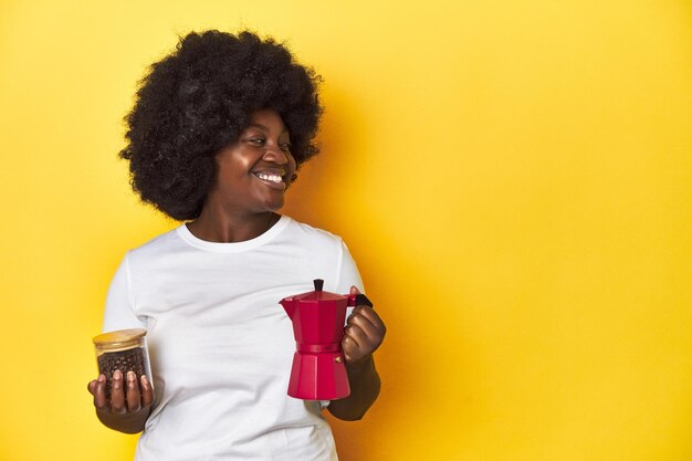 Foto mujer afroamericana sosteniendo una cafetera y frijoles premium en un fondo amarillo