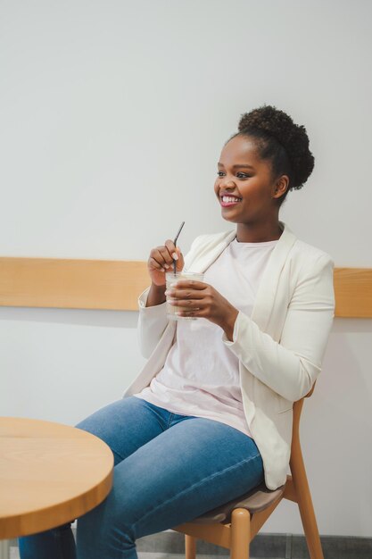 Mujer afroamericana sosteniendo un vaso de café helado sentado en la silla en una cafetería por la mañana El concepto de una bebida fría de verano