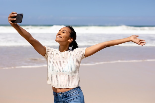 Mujer afroamericana tomando un selfie con smartphone en una playa junto al mar. estilo de vida saludable, ocio en la naturaleza.