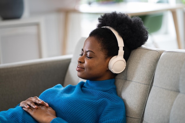 Una mujer afroamericana tranquila escuchando música con auriculares inalámbricos mintiendo con los ojos cerrados