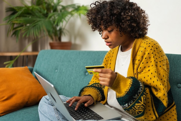 Mujer afroamericana usando computadora portátil comprando en línea pagando con tarjeta de crédito de oro chica sentada en