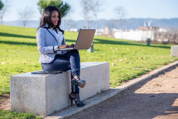 Mujer afroamericana usando una computadora portátil en un parque al aire libre