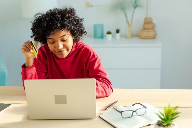 Mujer afroamericana usando laptop comprando en línea pagando con tarjeta de crédito dorada chica sentada en hom