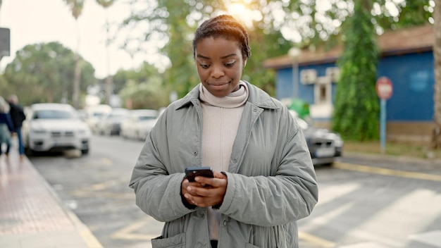 Mujer afroamericana usando un teléfono inteligente con una expresión seria en la calle