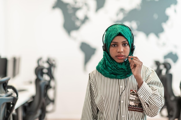 Mujer afromusulmana con pañuelo verde hiyab representante del cliente mujer de negocios con auriculares de teléfono ayudando y apoyando en línea con el cliente en un centro de llamadas moderno. foto de alta calidad