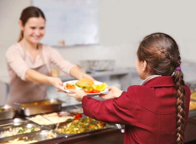 Mujer agradable dando el almuerzo a la niña de la escuela en la cafetería.