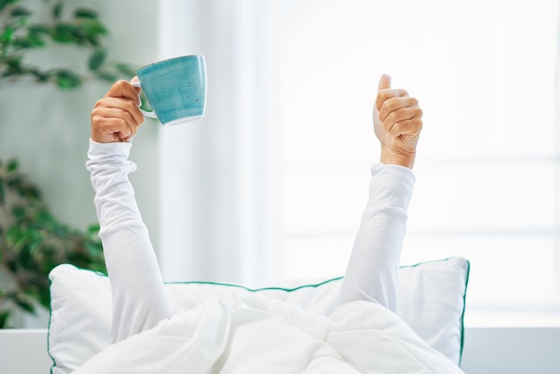 Mujer agradable joven en la cama con una taza de café o té