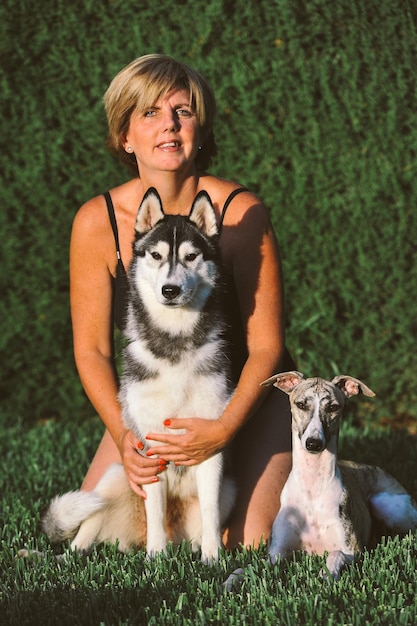 Una mujer agradable sentada en el jardín cerca del husky siberiano y el perro de pura raza whippet