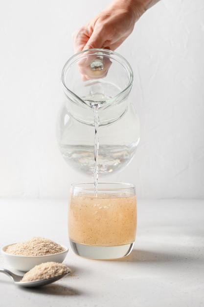 La mujer agrega fibra de psyllium al vaso de agua sobre un fondo blanco