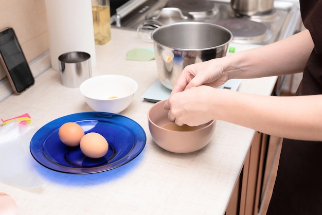 Mujer agregando claras de huevo en un tazón haciendo pastel de merengue casero Pavlova por receta en línea desde su teléfono Enfoque selectivo Proceso de concepto de cocina en casa